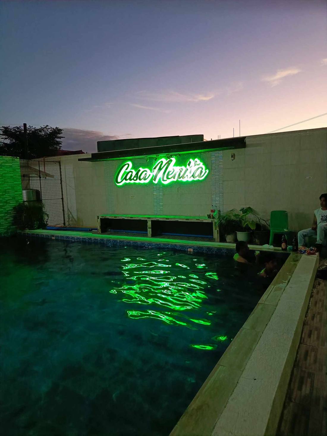 The pool lit green at dusk beneath the neon Casa Nenita sign
